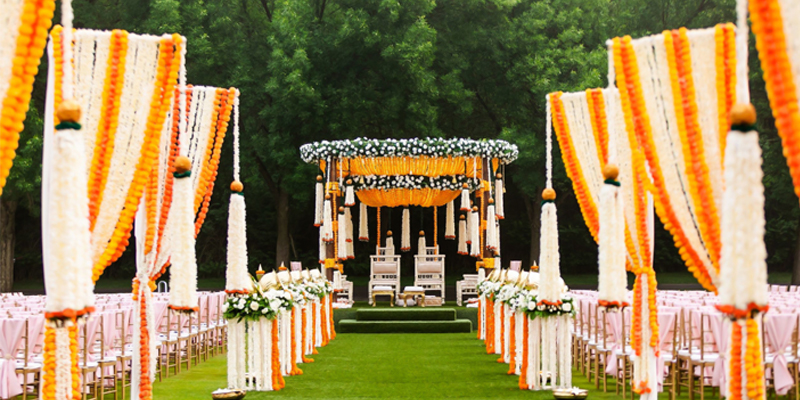 An Indian wedding mandap decorated with yellow and white flowers on an open lawn