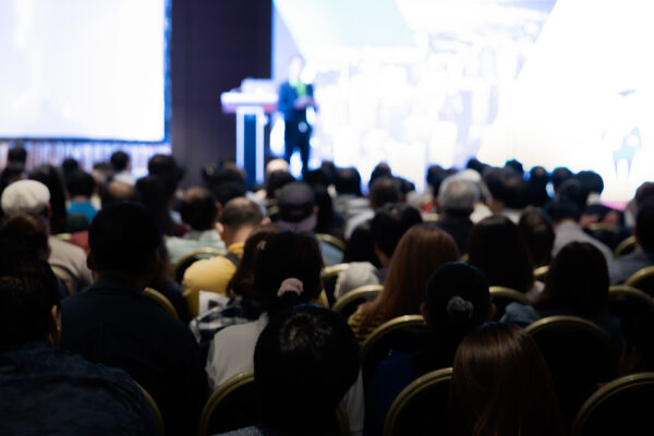 Rear view of a gathering of attendees in a conference hall for a corporate event.