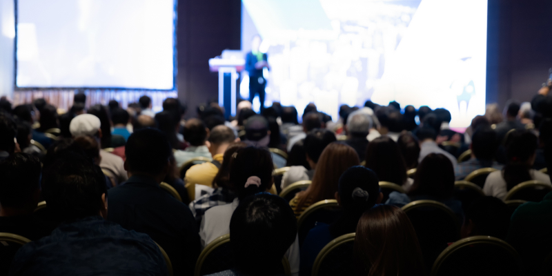 Rear view of a gathering of attendees in a conference hall for a corporate event.