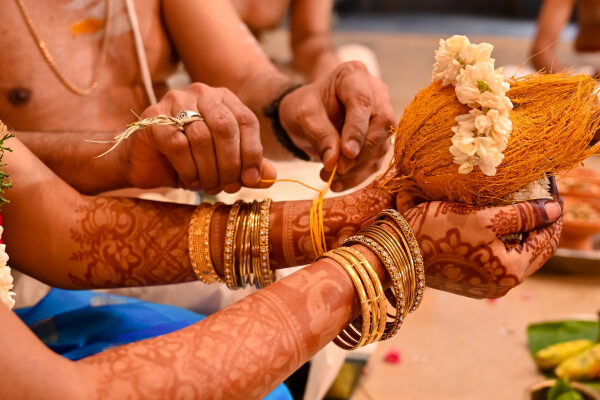 A bride securing a traditional kaapu, a Tamil Brahmin wedding ritual, around her wrist.