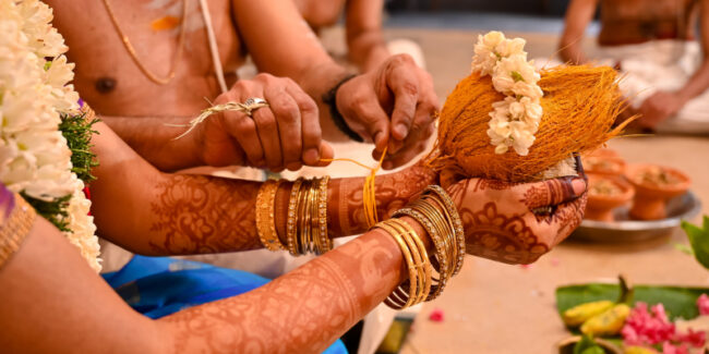 A bride securing a traditional kaapu, a Tamil Brahmin wedding ritual, around her wrist.
